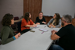 Students and faculty sit around a table during a work session.