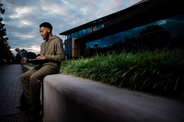 An IU student works on a laptop outside at dusk