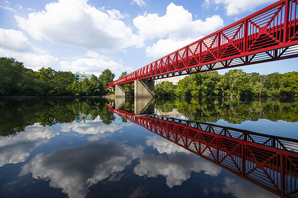 The red pedestrian bridge at IU South Bend spans a river, which reflects trees and the sky.