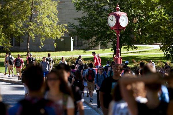 Large group of students walking in front of red clock tower on IU Bloomington campus.